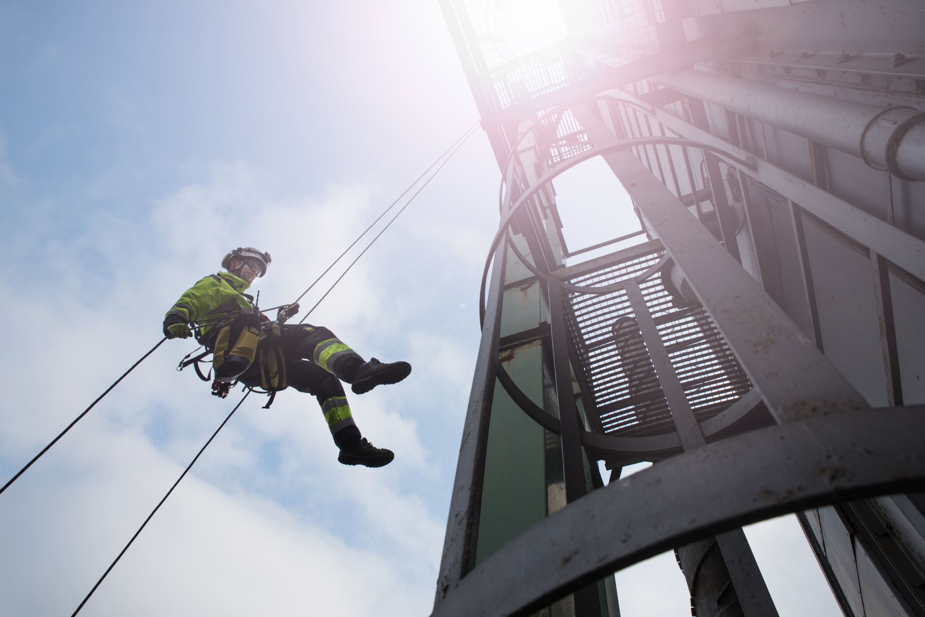 Trabalhador com equipamento de segurança em rapel de alto da torre.