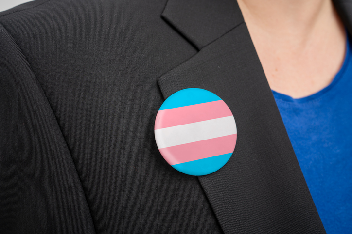 Na imagem uma mulher com um broche representando a bandeira trans