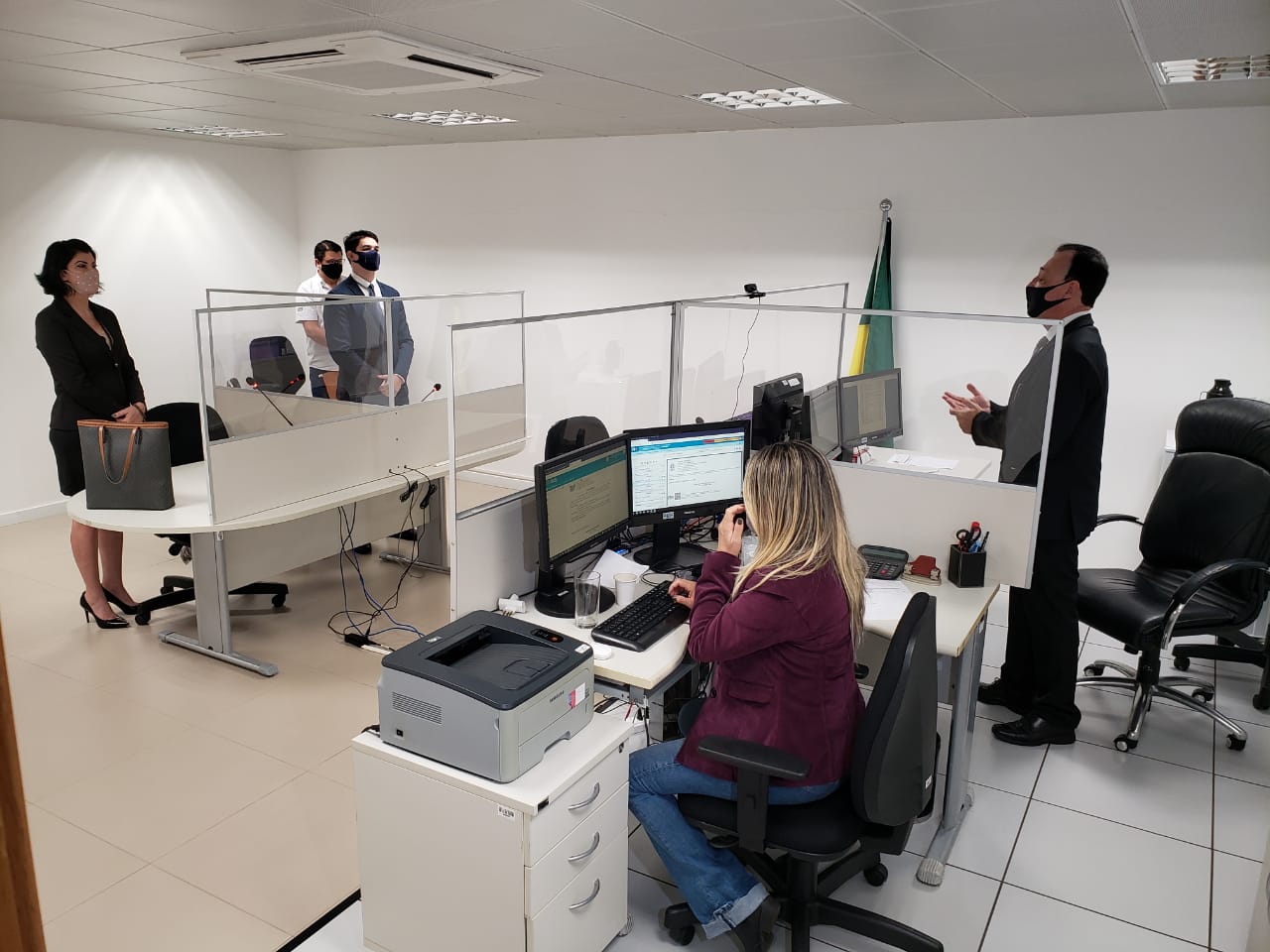 A fotografia demonstra as adaptações realizadas em uma sala de audiência por conta das condições instauradas pela pandemia. Anteparos de acrílico separam as mesas de cada um dos trabalhadores.