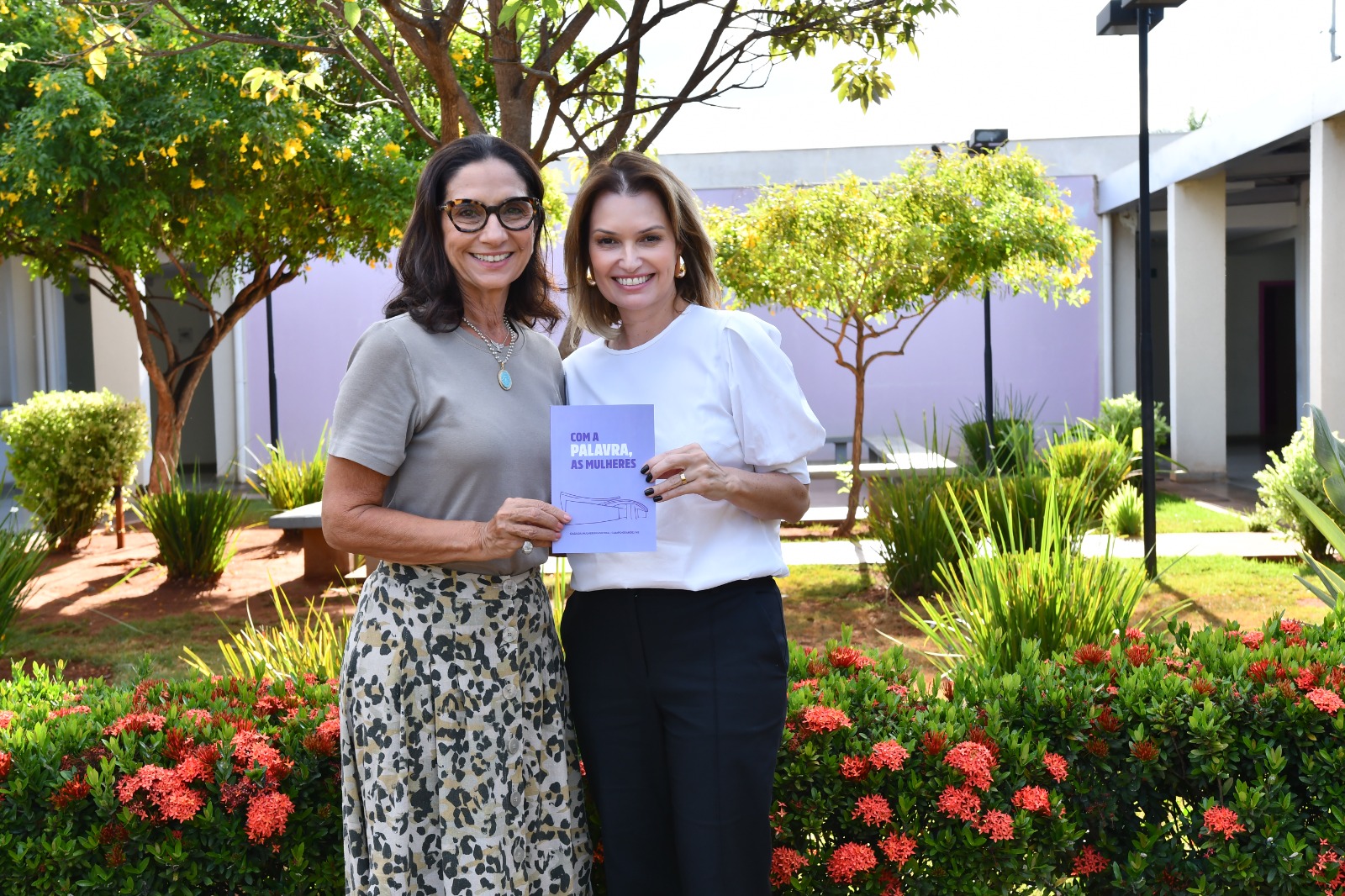 Carla entrega livro para juíza Ana Paola em jardim da casa da mulher