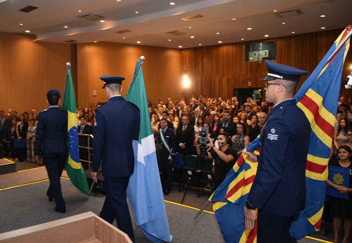 Foto de militares da Força aérea no palco. Andam enquanto seguram bandeiras do Brasil, Estado de MS e da cidade de Campo Grande.